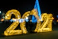 Defocused silhouettes of big golden 2021 figures New Years holiday lights. Blurry street New Year`s light installation