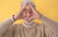 Defocused smiling senior bearded man making heart shape with his hands on yellow background