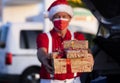 Defocused smiling senior bearded man shopping for Christmas in a Santa hat and suspenders, holding gifts and looking at camera