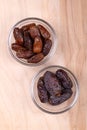 Deglet Nour and Medjool dates, in glass bowls, on a wooden panel, from above