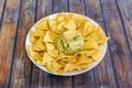 45 degree image of plate of corn nachos with green mexican guacamole on dark wood background