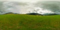 360 by 180 degrees spherical panorama of a cows grazing on green grass in mountainous natural landscape with cloudy sky