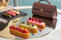 Delectable eclairs with fresh berries are displayed on a reflective surface beside a designer handbag Royalty Free Stock Photo