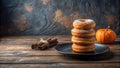 A delectable stack of four sweet, sugar-dusted donuts rests on a dark plate, accompanied by a small pumpkin and a bundle of Royalty Free Stock Photo