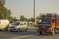 Indian red truck and gray passenger car in city traffic en against the background of green trees and the