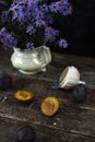 Delicate blue flowers in white vase near orange plum