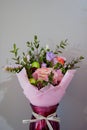 A delicate bouquet of different flowers in a light pink wrapper stands in a burgundy vase on a gray background Royalty Free Stock Photo