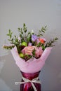 A delicate bouquet of different flowers in a light pink wrapper stands in a burgundy vase on a gray background. Royalty Free Stock Photo