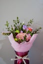 A delicate bouquet of different flowers in a light pink wrapper stands in a burgundy vase on a gray background. Royalty Free Stock Photo