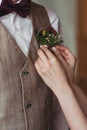 Delicate bride`s hands adjust groom`s boutonniere