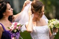 Delicate bridesmaid helps a bride to put on a wedding veil