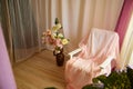 Delicate bright pink interior of the room with armchair, a vase with roses, draped curtains and a window. Location and