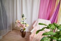 Delicate bright pink interior of the room with armchair, a vase with roses, draped curtains and a window. Location and