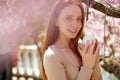 Delicate caucasian redhead woman posing in spring blossom flowers with cream in hands