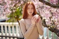 Delicate caucasian redhead woman posing in spring blossom flowers with cream in hands