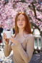 Delicate caucasian redhead woman posing in spring blossom flowers with cream in hands