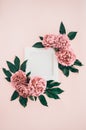 Delicate composition with wooden photo frame with white blank canvas and muted pink peony flowers with dark green leaves on the