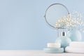 Delicate elegant ceramic decorations for bathroom - soft blue bowls, vase, white flowers, towel and soap on white wood table.