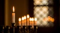 Delicate flame of a single candle on an antique Menorah with warm candlelight glow and patterned window reflection Royalty Free Stock Photo