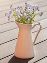 Delicate forget-me-not flowers in a white jug on a wooden background. Royalty Free Stock Photo