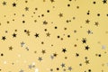 Delicate glitter star confetti on yellow background.