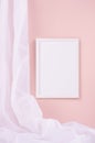 Delicate home decor with blank rectangle photo frame hanging on pastel pink wall, flow of silk curtain, vertical. Mock up. Royalty Free Stock Photo