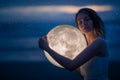 Delicate image of an angel, a girl with the moon in her hands on the night beach. artistic photography. Fairy tale and riddle.