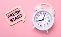 On a delicate pink background, a white alarm clock and a wooden frame with the text FRESH START