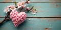 Delicate pink knitted heart resting on rustic weathered wood beside a branch of spring blossoms. Generative AI Royalty Free Stock Photo