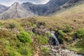 A delicate waterfall cascades into the Fairy Pools, surrounded by Isle of Skye\'s lush terrain and distant Cuillin mountains