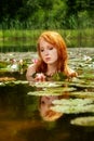 Delicate young red-haired woman delights sensual in the water on a pink water lily flower Royalty Free Stock Photo