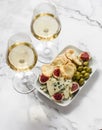 Delicious aperitif - appetizer plate with blue cheese, olives, homemade cheese cracker, figs and two glasses of white wine on a