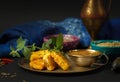 Cheese in mint batter with chutney sauce, an Indian dish. On a copper plate with fresh mint, bowls of spices in the background.