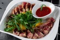 Delicious appetizer with sliced bacon, arugula, orange and red sauce on grey table. Traditional dish menu served in a restaurant, Royalty Free Stock Photo