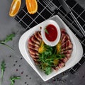 Delicious appetizer with sliced bacon, arugula, orange and red sauce on grey table. Traditional dish menu served in a restaurant, Royalty Free Stock Photo