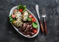 Delicious appetizer, tapas, lunch plate - beef steak, vegetables salad and baked potatoes with blue cheese on a dark background, Royalty Free Stock Photo