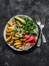Delicious appetizer, tapas plate - french fries, salmon, arugula, gherkins, olives on a dark background, top view Royalty Free Stock Photo