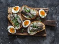 Delicious appetizer, tapas - soft boiled eggs and canned sardines sandwiches on a cutting board on a dark background, top view Royalty Free Stock Photo