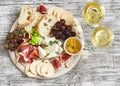 Delicious appetizer to wine - ham, cheese, grapes, crackers, figs, nuts, jam, served on a light wooden board, and two glasses with