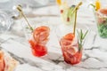 Delicious appetizers in glass cups with ham meat and tomato on marble banquet table. Catering food, canape and snacks, close up.