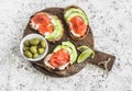 Delicious appetizers with wine - cream cheese, smoked salmon and avocado sandwiches and olives on a wooden board.