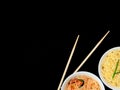 Delicious asian curly noodles and funchose salad in white bowls with wood sticks on black background. Selective focus Royalty Free Stock Photo