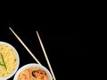 Delicious asian curly noodles and funchose salad in white bowls with wood sticks on black background. Selective focus Royalty Free Stock Photo