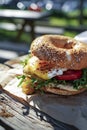 A delicious bagel sandwich with fresh vegetables, melted cheese, and a sunny-side-up egg, served outdoors on a wooden surface Royalty Free Stock Photo