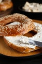 Delicious bagel with tofu cream cheese and knife on black wooden table, closeup