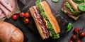 Delicious baguette sandwich with ham, bacon, cheese, lettuce, tomatoes, sausage, gammon on cutting board Royalty Free Stock Photo