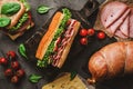 Delicious baguette sandwich with ham, bacon, cheese, lettuce, tomatoes, sausage, gammon on cutting board Royalty Free Stock Photo