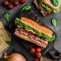 Delicious baguette sandwich with ham, bacon, cheese, lettuce, tomatoes, sausage, gammon on cutting board Royalty Free Stock Photo