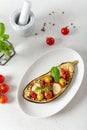 Delicious baked eggplant. Aubergine stuffed with vegetables, olives and cheese on a white plate. Top view, close up, vertical. Royalty Free Stock Photo