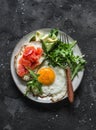 Delicious balanced breakfast - egg, salmon sandwich, avocado and arugula on a dark background, top view